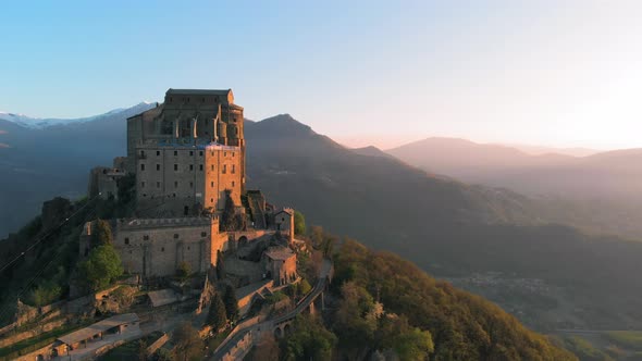 Aerial: drone flying at old medieval abbey perched on mountain top at sunrise, Turin italian Alps