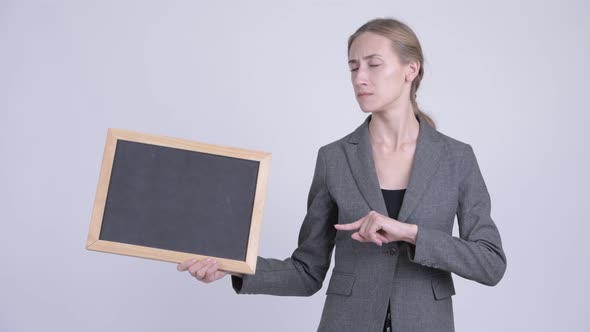 Serious Young Blonde Businesswoman Holding Blackboard and Giving Thumbs Down