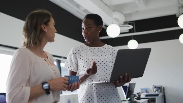 Two diverse female colleagues looking at laptop and discussing in office