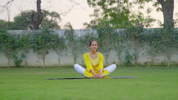 Butterfly Yoga Pose or Titliasana is being done by an Indian woman in a park