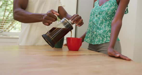 Midsection of african american couple in kitchen pouring coffee from cafetiere