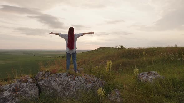 Back Side of a Girl on the Stone Raises Her Hands to the Sky