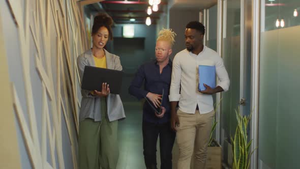 Diverse business people discussing with laptop and walking in creative office