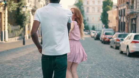 Young Happy Woman Leads Her Boyfriend's Hand Along City Street Rear View