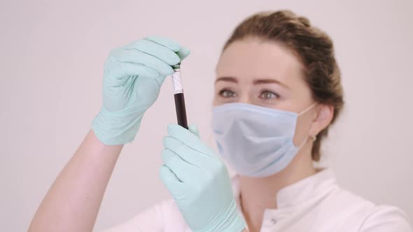 Female Doctor in Mask Looking at Blood Sample with Coronavirus