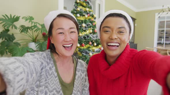 Happy diverse female friends in santa hats making christmas video call, blowing kisses and smiling