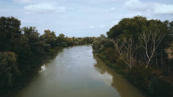 Drone shot of muddy slow river between fields and trees