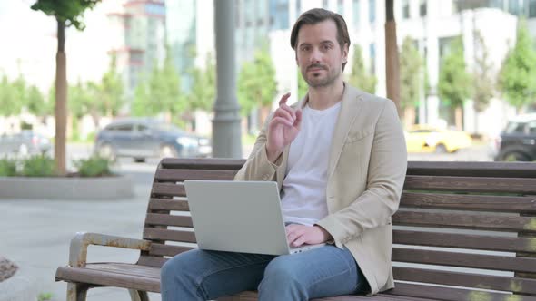 Young Man Pointing at the Camera While Sitting on Bench Outdoor