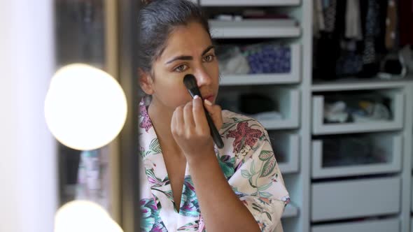 Young woman applying makeup under eyes in bedroom