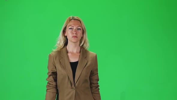 Blonde Girl in a Stylish Brown Jacket Going and Looking Straight Into the Camera Against a Green