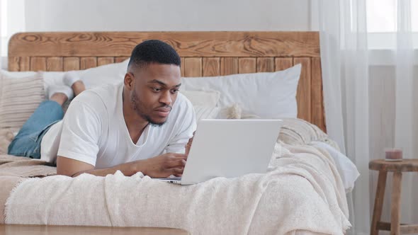 Afro American Man Ethnic Student Black Mixed Race Freelancer Sits Lies on Bed with Laptop Looks Into