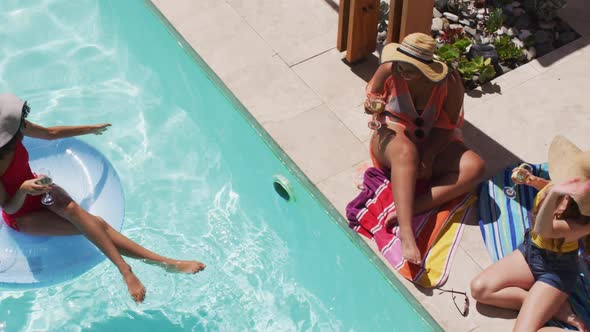 Diverse group of female friends wearing straw hats having fun raising one's glasses at pool