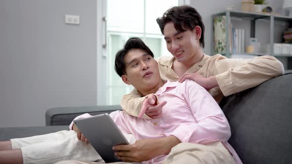 Young happy lgbtq couple Lying Down on a Sofa and Use a tablet, doing online shopping together