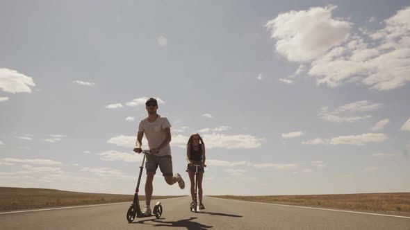 The Young Guy with the Girl Riding on Scooters on an Empty Highway