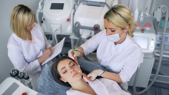 Cosmetologist Makes the Procedure Microcurrent Therapy of the Facial Skin of a Beautiful Young Woman