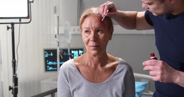 Artist Making Fake Bloody Wound on Senior Female Forehead