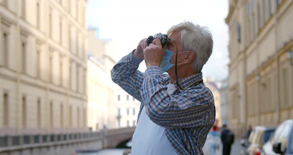 Senior Man Tourist in Safety Mask Taking Pictures on Vintage Camera in City