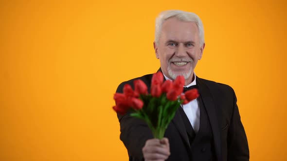 Senior Gentleman Presenting Tulips Bouquet and Smiling, Sincere Greeting Holiday