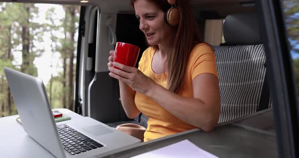 Senior caucasian woman using laptop and wireless headphone inside mini van camper