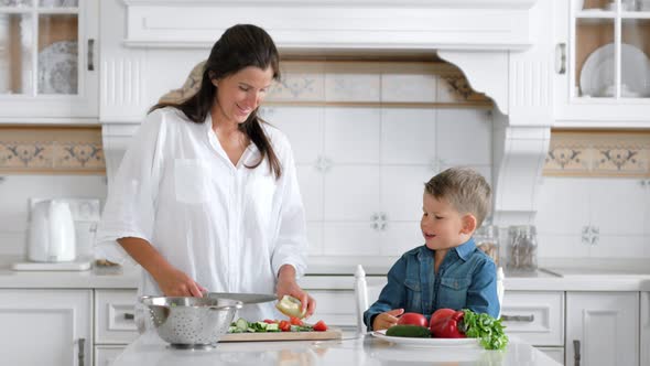 Medium Shot Little Boy Helping His Mother While Cooking Salad Using Knife and Board at Home Kitchen