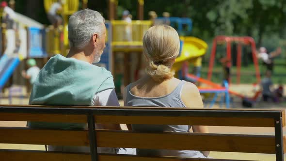 Retired Man and Woman on Bench in Park Watching Grandchildren, Happy Memories