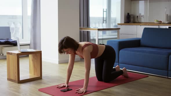 Young Sporty Lady Turning on Timer on Smartphone and Start Doing Plank Exercise