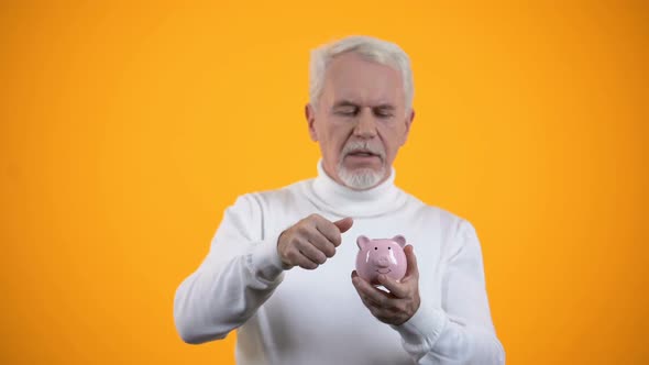 Aged Man Putting Coin and Shacking Piggy Bank, Savings and Budget, Finance