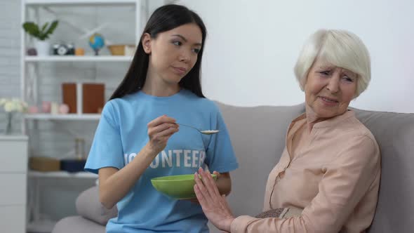 Upset Elderly Woman Refusing to Eat Oatmeal Offered by Volunteer, Nursing Home