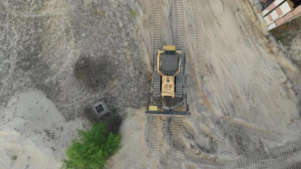 Top Aerial View on Tracked Bulldozer Rides on Sandy Road at Construction Site