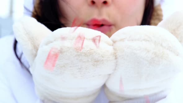 A woman blows red sequins in the shape of hearts from warm fur mittens
