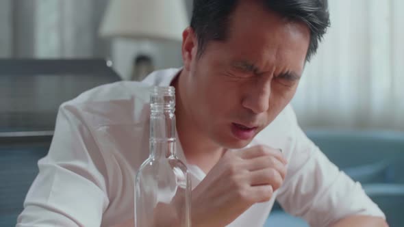 Close Up Of Drunk, Depressed Asian Man Pouring Vodka In A Shot Glass Before Drinking At Home
