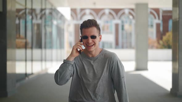 Handsome Caucasian Man with in Sunglasses Walks and Speaks on a Mobile Phone in a City Park.