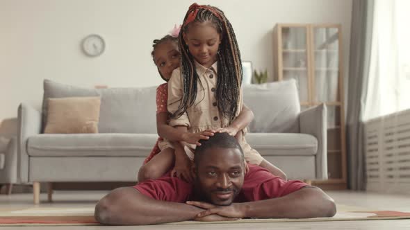 Daughters Sitting on Dad Lying on Floor