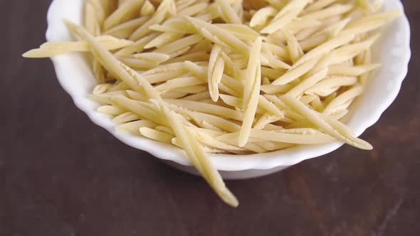 Falling raw Italian trofie pasta in slow motion into a white bowl