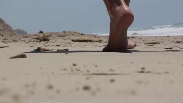 Low angle view of a man's bare foot walking on the beach dressing summer clothes.