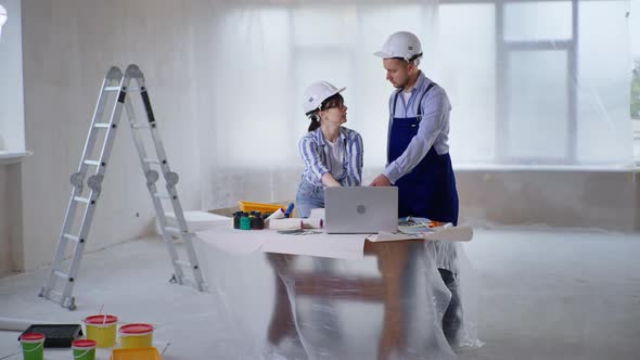 Female Designer with Construction Worker in Safety Helmets Discussing Paint for Walls Choosing Shade