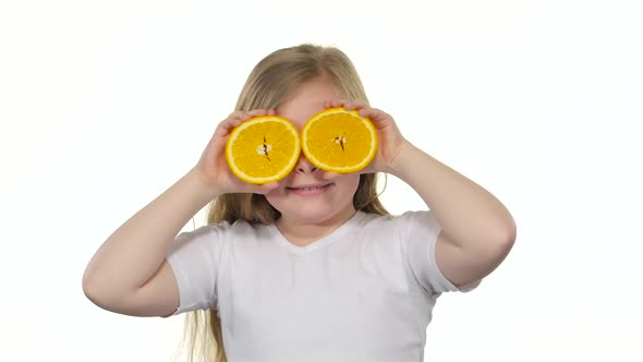 Little Girl Holding an Orange Slice Closes Her Eyes and Curves. White Background