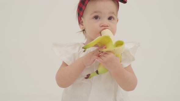 Little girl in plaid headband and skirt is eating big banana