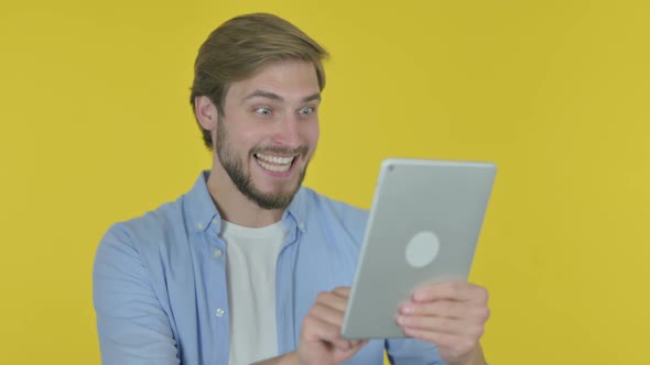 Young Man Celebrating Success on Tablet on Yellow Background