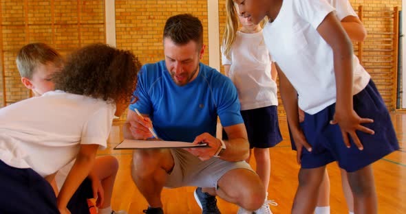 Sports teacher and schoolkids discussing over clipboard in the basketball court 4k