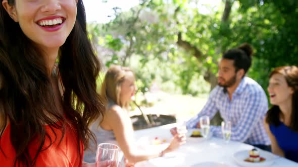 Portrait of woman standing with champagne glass while friends interacting in background