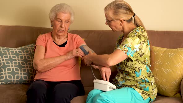 Home healthcare nurse and elderly woman taking blood pressure with a machine.