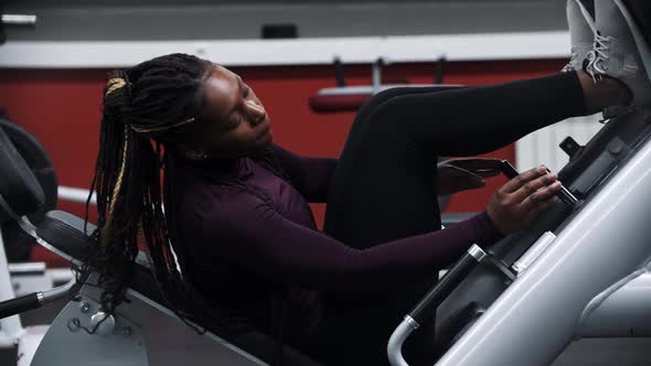 A Black Woman with Braids Setting Up a Exercise Equipment for Legs