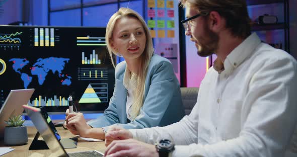 Man and Woman Browsing Charts on Tablet PC while Working Overtime in the Office in the Evening