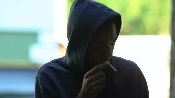 Hooded black male teenager secretly smoking, hiding from parents