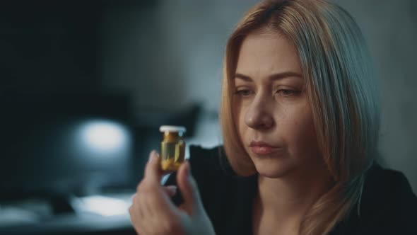 Pensive Woman Holds Glass Pill Bottle in Semidark Office