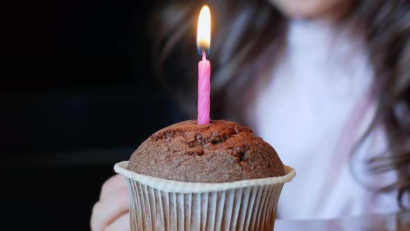 Child blows out a burning candle on a birthday cupcake. Birthday. alt