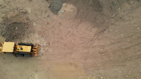 Aerial flyover of a construction grader in a dirt lot.