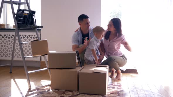 Merry Family with Small Son Enjoys New Light Home After Repairs Among Cardboard Boxes with Things