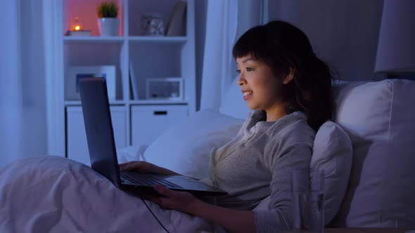 Woman with Laptop in Bed at Home at Night